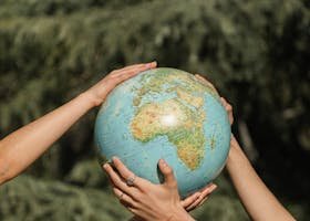 Four hands holding a globe outdoors, symbolizing unity and environmental conservation.